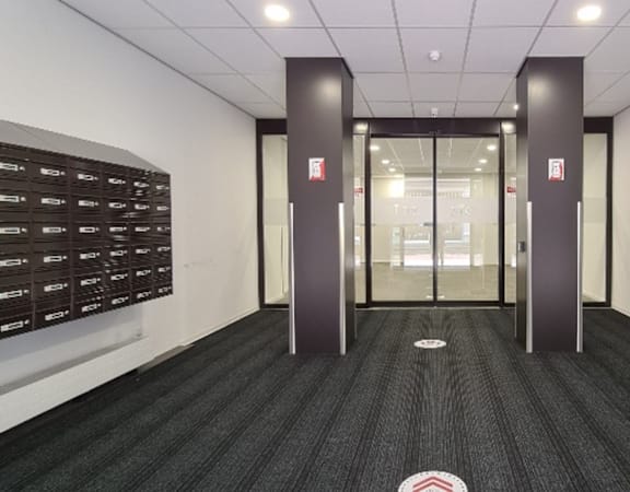 A hallway with a black carpet and white walls with a glass door in the middle.