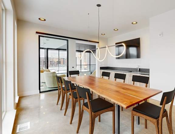 A long wooden dining table with chairs and a chandelier hangs in a white room.