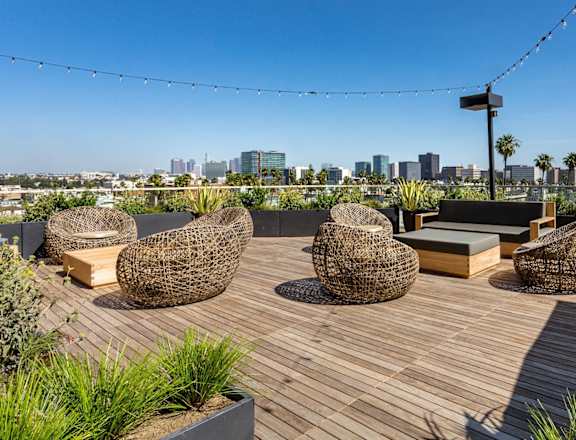 A rooftop patio with wicker chairs and a city skyline in the background.
