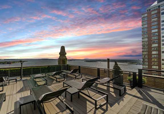 A rooftop patio with a table and chairs overlooking the water. at One West,  New York,10004