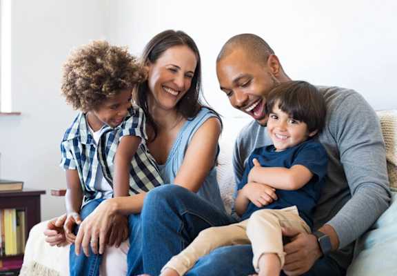 A family of four is sitting on a couch together.