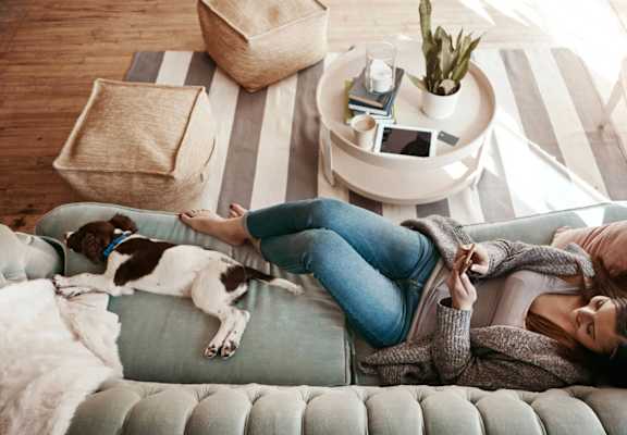 A woman is lying on a couch with her dog.