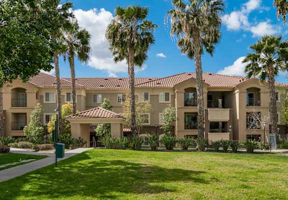 A building with a red tile roof and palm trees in front.