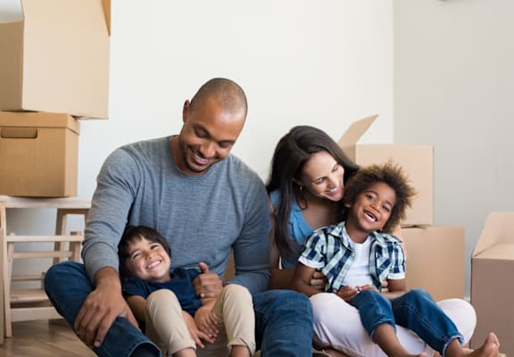 A family of four sitting together surrounded by moving boxes.