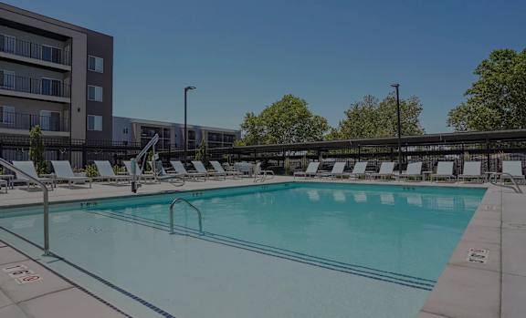 A sunny day at the pool with lounge chairs and a building in the background.