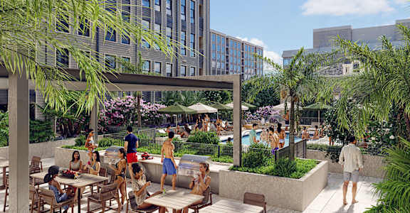A group of people are sitting and standing on a patio with a pool.