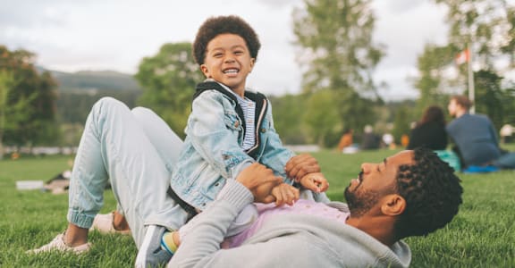 A man and a child are lying on the grass in a park.