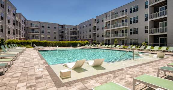 A large outdoor swimming pool surrounded by lounge chairs and buildings.