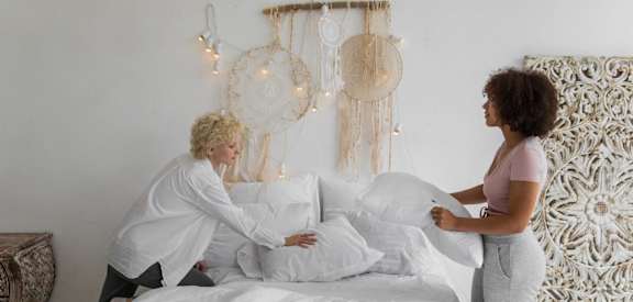 Two women are making a bed together.
