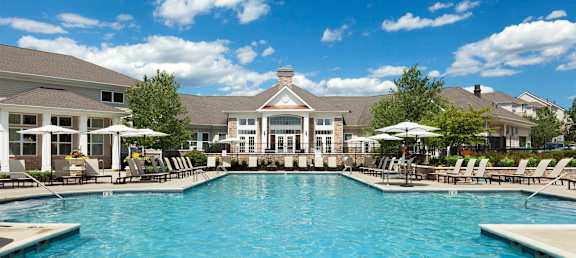 a large swimming pool with chairs and umbrellas in front of a house