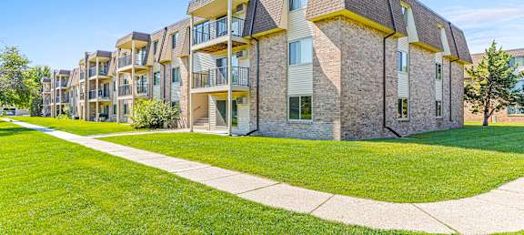 an exterior view of an apartment building with green grass and a sidewalk