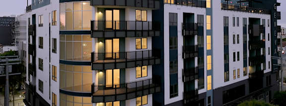 A modern building with a curved design and balconies is illuminated from within.