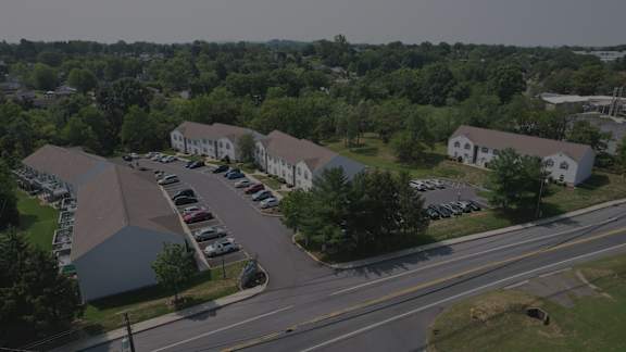 A parking lot is surrounded by trees and houses.