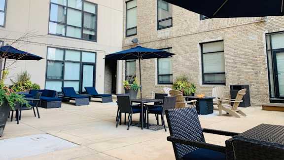 A patio with black chairs and tables is surrounded by a building.