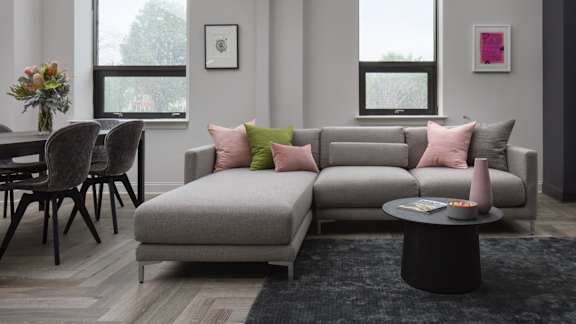 A grey couch with pink and green pillows sits in a living room.