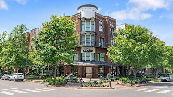 A large brick building with a round top is surrounded by trees and has a street in front of it.