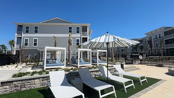 A white striped umbrella is in the middle of a patio with white chairs.