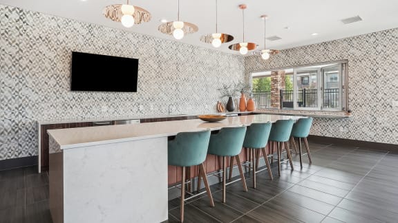 a kitchen with a long bar with blue chairs and a television