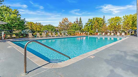 our resort style swimming pool is surrounded by lounge chairs and trees