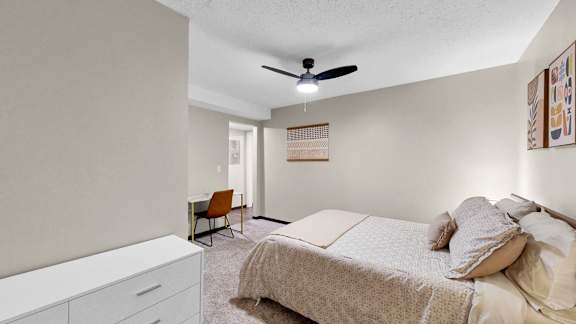 A bedroom with a bed, chair, and ceiling fan.