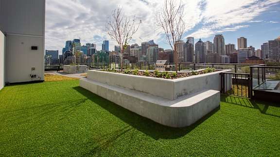 a view of the city from a roof top terrace with grass and a bench