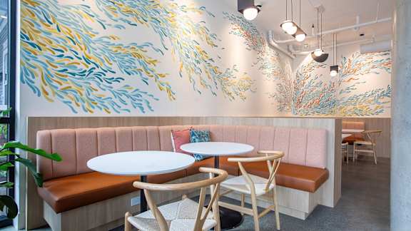 a dining room with two tables and a pink couch and a mural on the wall