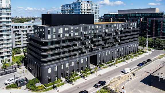A large black building with many windows is surrounded by other buildings and a parking lot.