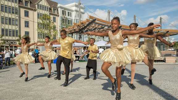 A group of dancers in gold dresses are performing on a stage.