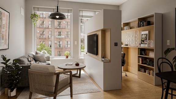 A living room with a grey couch, a brown chair, a coffee table, a bookshelf, and a window with a view of a building outside.