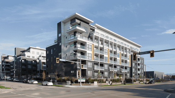 A modern multi-story building with balconies and a parking lot in front.