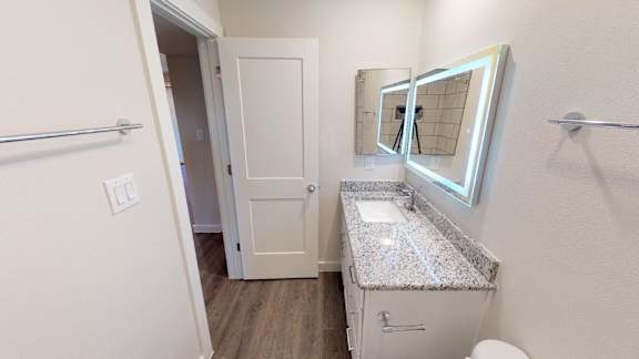 A bathroom with granite vanity and LED lit mirror.