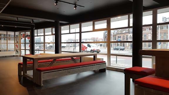 A room with a long table and benches with a view of the street outside.