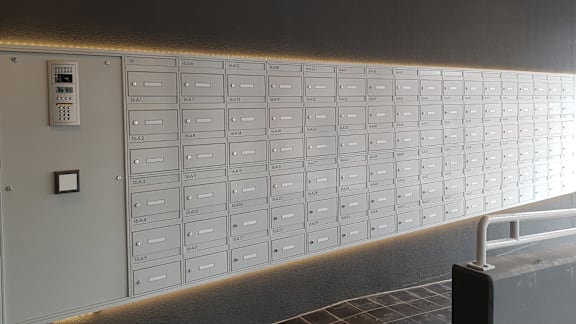 A wall of mailboxes with a control panel on the wall.
