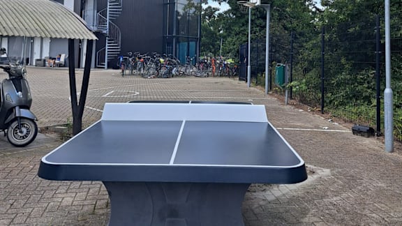 A grey table tennis table in the middle of a brick courtyard.