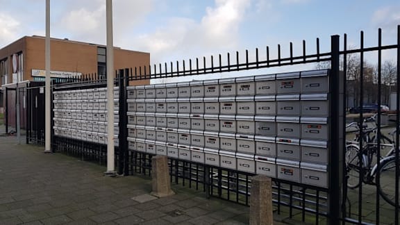 A row of mailboxes are lined up on a black fence.