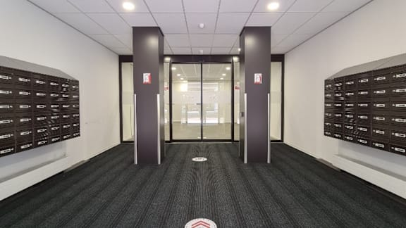 A hallway with a black carpet and white walls with a glass door in the middle.