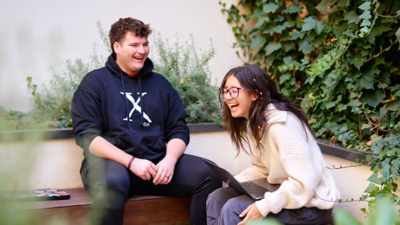 a man and a woman sitting on a bench with their laptops