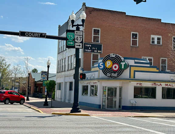 A red car is parked on the side of the road in front of a building with a sign that reads "PIE MALIS".