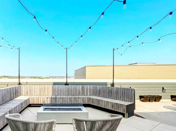 A patio with a bench, chairs, and string lights.