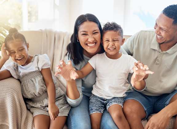 Smiling family sitting on a couch at The Groves Apartments, Raleigh, North Carolina