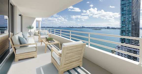 A balcony with a couch, chairs and a table with a view of the water and buildings.