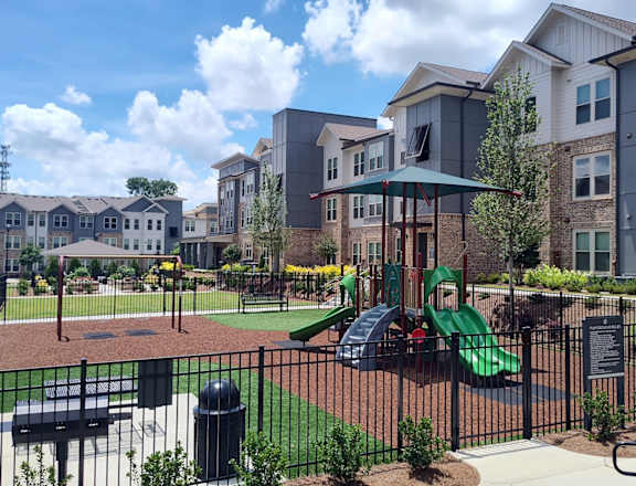 A playground with a green slide and a black fence.