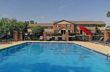 A swimming pool in front of a brick building with a red umbrella.