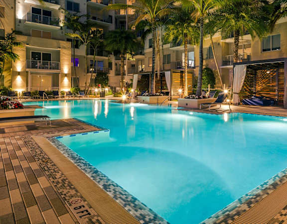 A large swimming pool surrounded by palm trees and a building.