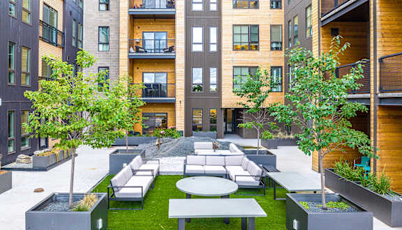 A modern courtyard with a grassy area, trees, and a white sofa.