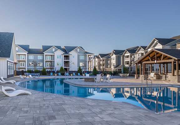 A swimming pool surrounded by a patio and lounge chairs in front of a row of houses.