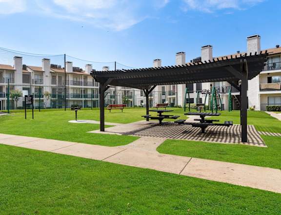 a park area with picnic tables and awning in front of an apartment building