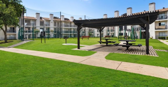 a park area with picnic tables and awning in front of an apartment building