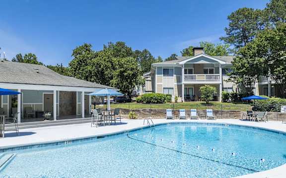 A swimming pool in front of a house with a blue umbrella.