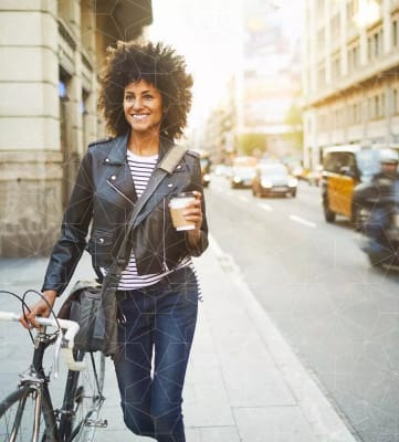 a woman walking her bike down the street with a cup of coffee